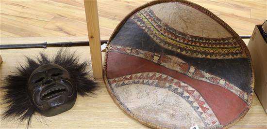 An Asian mask, a Masai hide shield and spear shield length 75cm approx.